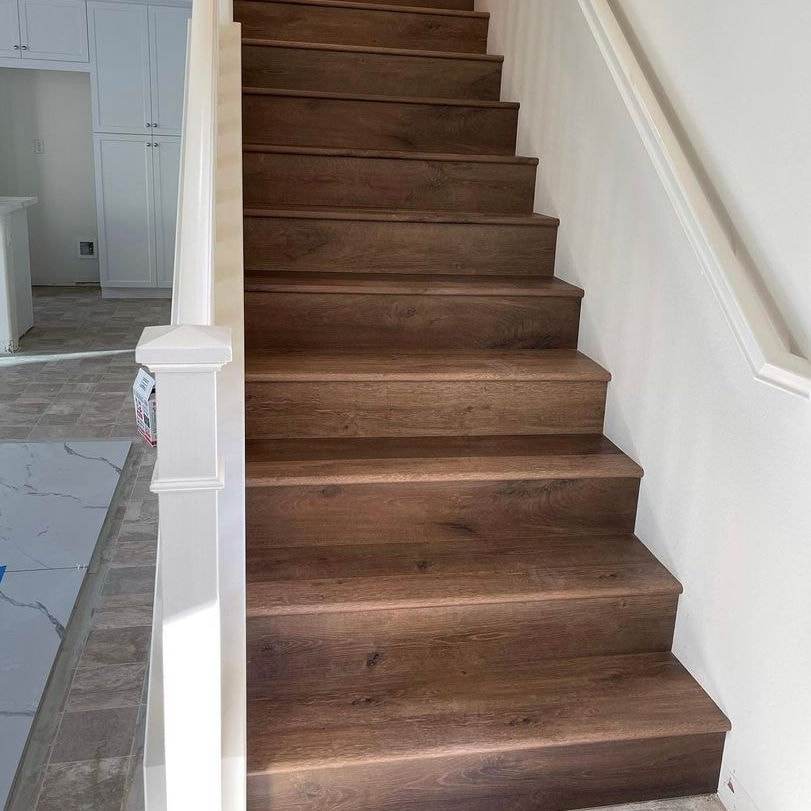Escalera con peldaños de madera oscura y contrahuellas blancas en una casa