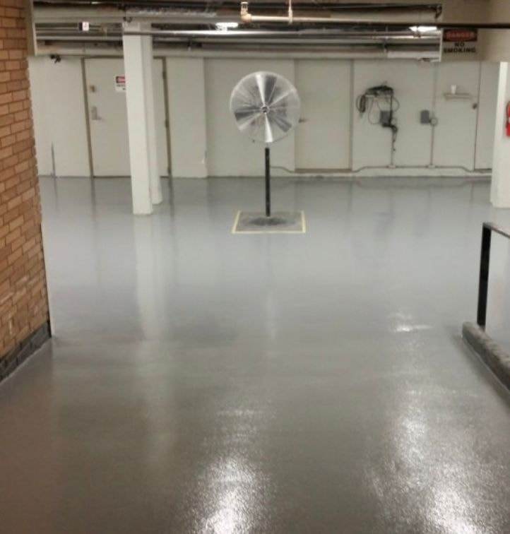 Piso epóxico gris en un edificio industrial, con un ventilador de pie